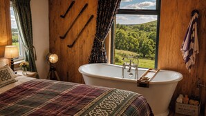 A bedroom with a large bed, a white bathtub, and a window with a view of a green landscape. - Seaside Retreat Cottage in Carrowmenagh (Carrowmenagh)