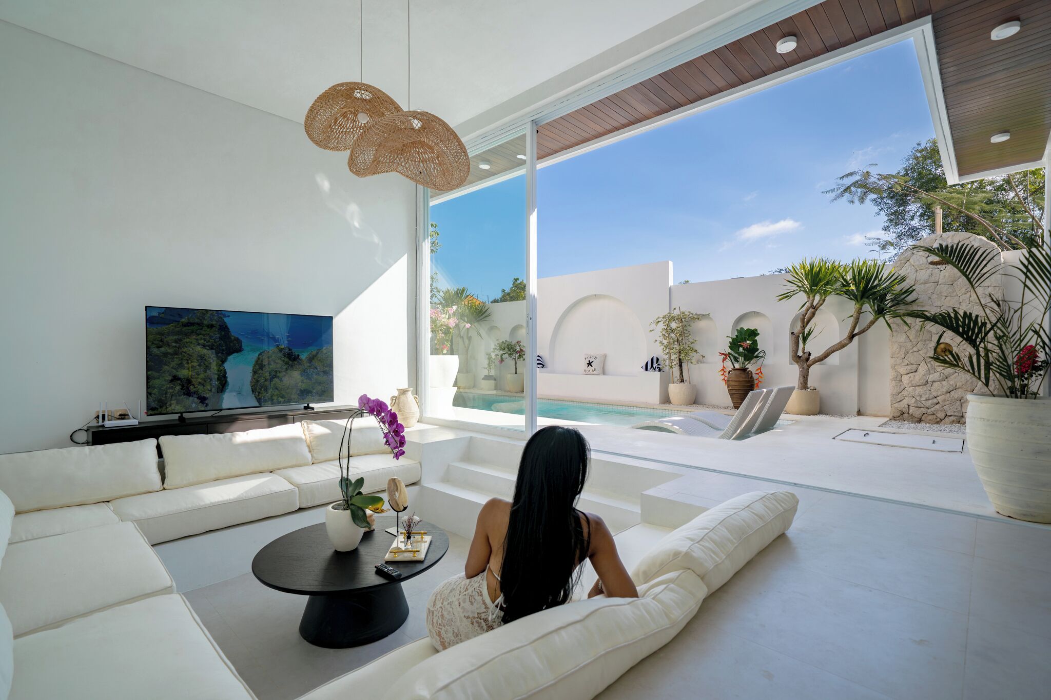 A modern living room with a white sofa, a coffee table, and a TV on the wall.