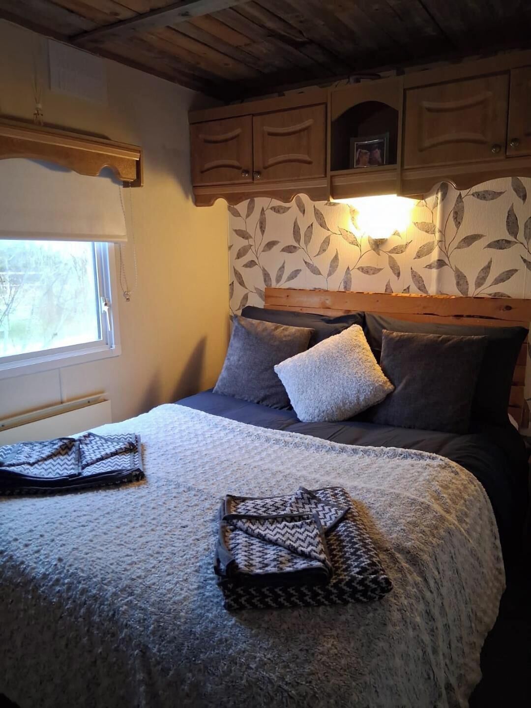 Une chambre à coucher avec un lit, des oreillers, une tête de lit, une fenêtre et des armoires en bois.