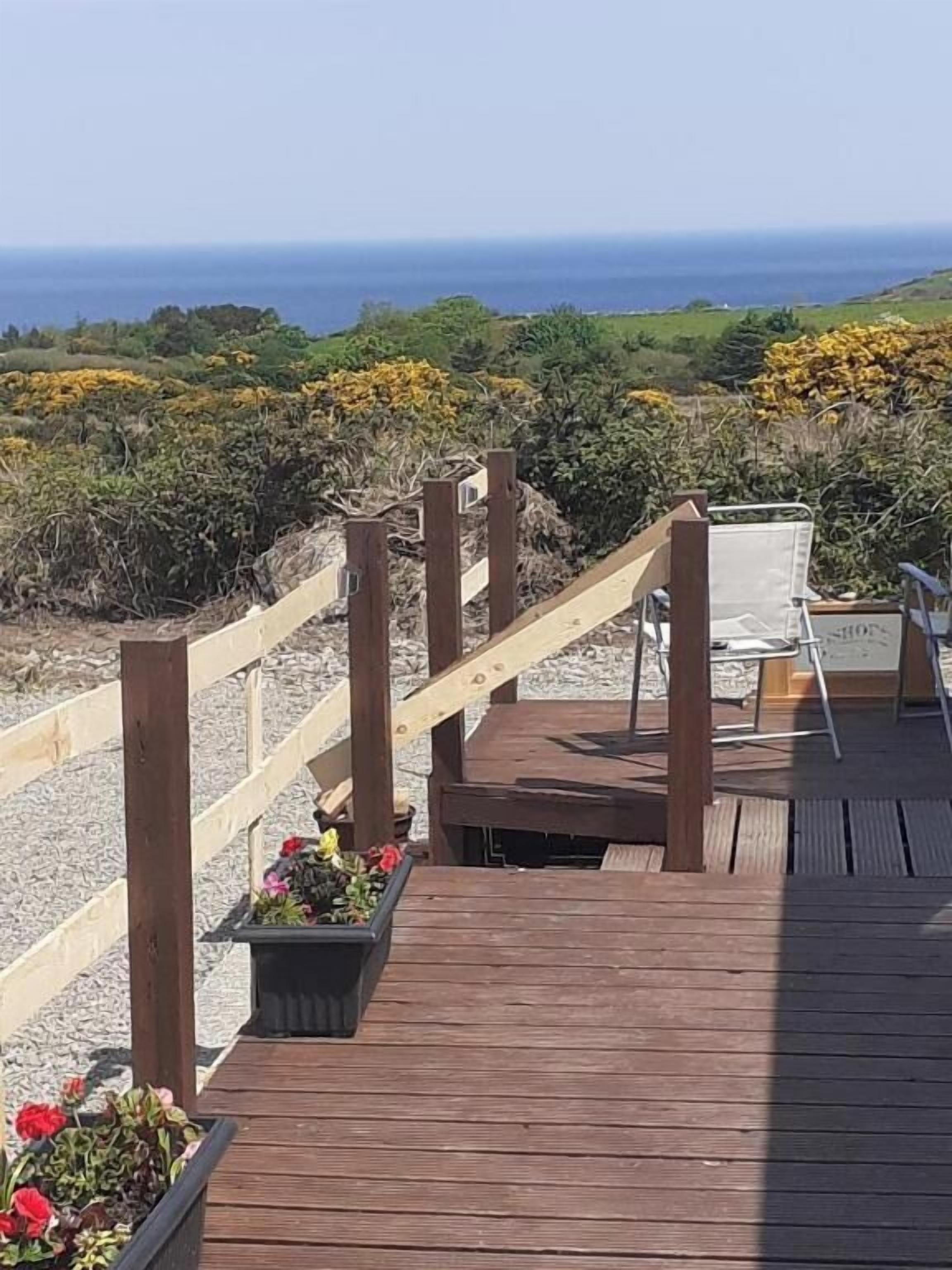 Une terrasse en bois avec une chaise et une table, offrant une vue sur un paysage côtier.
