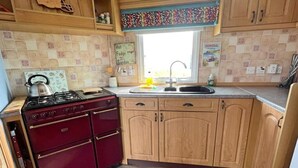 A kitchen with wooden cabinets, a gas stove, and a window above the sink. - Cozy Carrowmenagh Cabin Retreat (Culdaff)