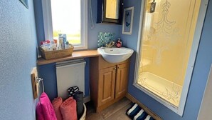A bathroom with a window, a sink, a mirror, and a shower with decorative glass. - Cozy Carrowmenagh Cabin Retreat (Culdaff)