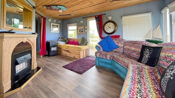 A cozy room with a fireplace, a sofa, a bed, and a wooden ceiling. - Cozy Carrowmenagh Cabin Retreat (Culdaff)