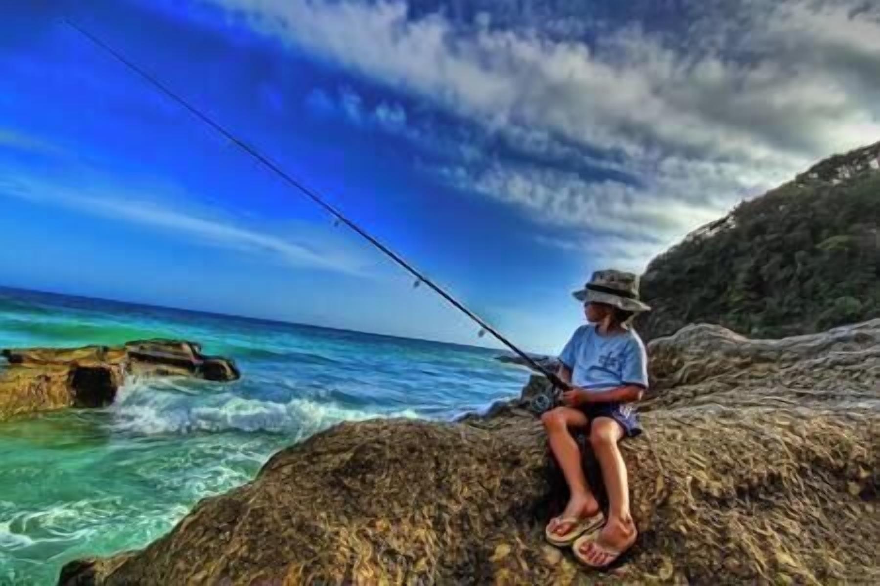 Une personne est en train de pêcher sur un promontoire rocheux au bord de la mer.