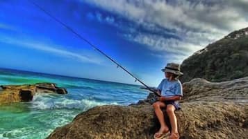 Une personne est en train de pêcher sur un promontoire rocheux au bord de la mer.