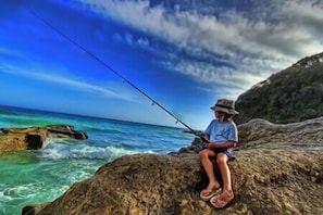 A person fishing on a rocky outcrop by the sea.