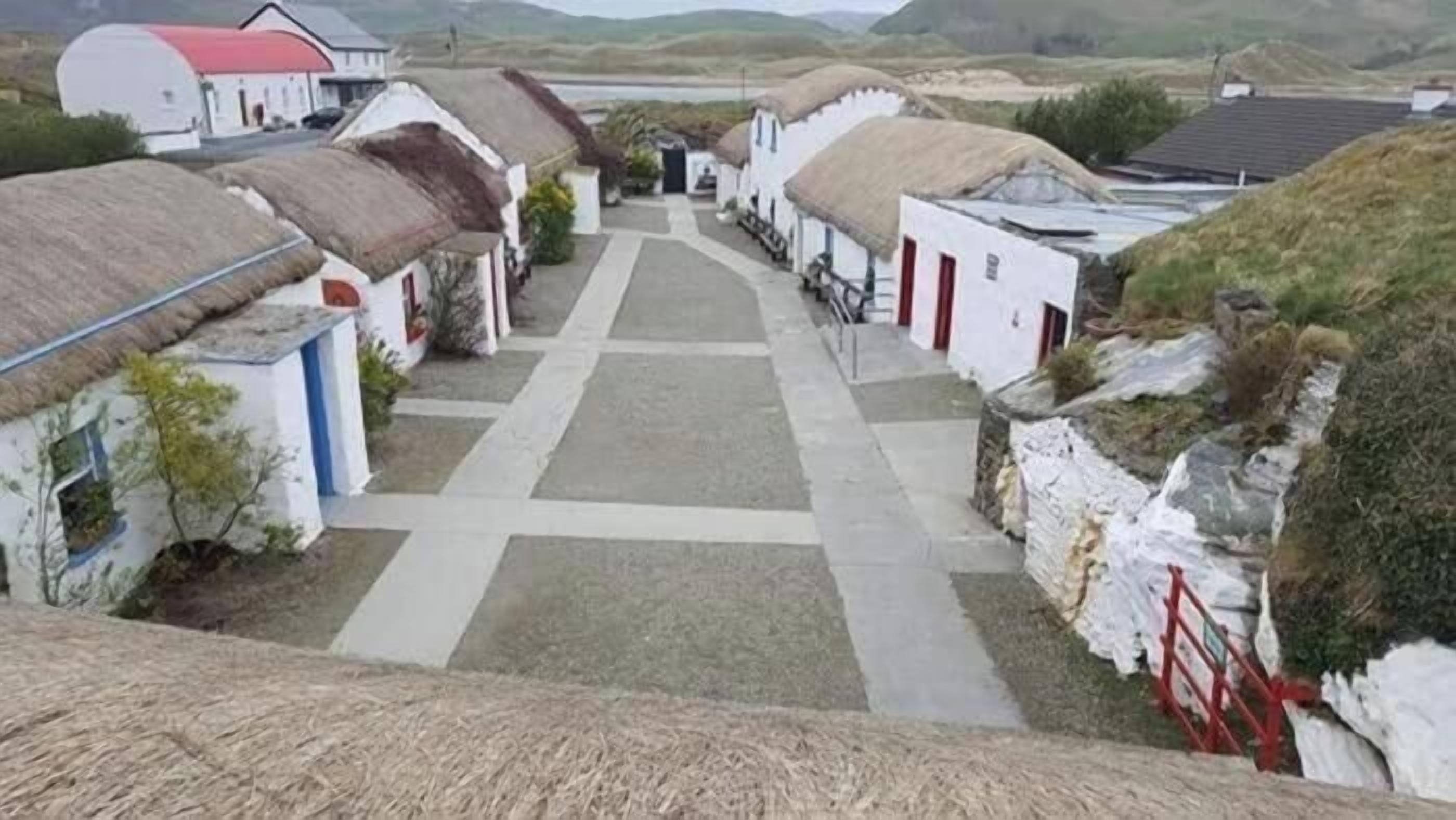 A village with thatched-roof cottages, a central pathway, and a body of water in the background.