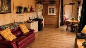 A cozy cabin interior with a wooden floor, a red leather sofa, a dining table, and a kitchen area. - Cottage Sleeps 4 with Parking and Sea Views (Carrowmenagh)