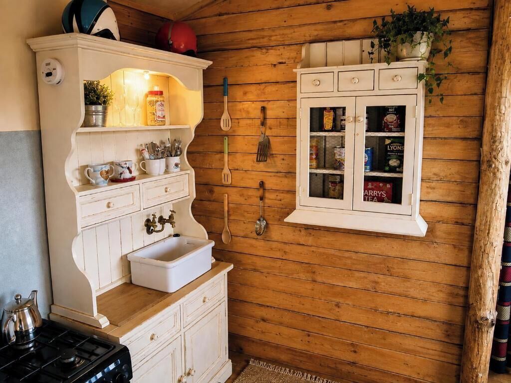 Une cuisine avec des meubles en bois, un évier blanc et une fenêtre où sont exposés des produits liés au thé.