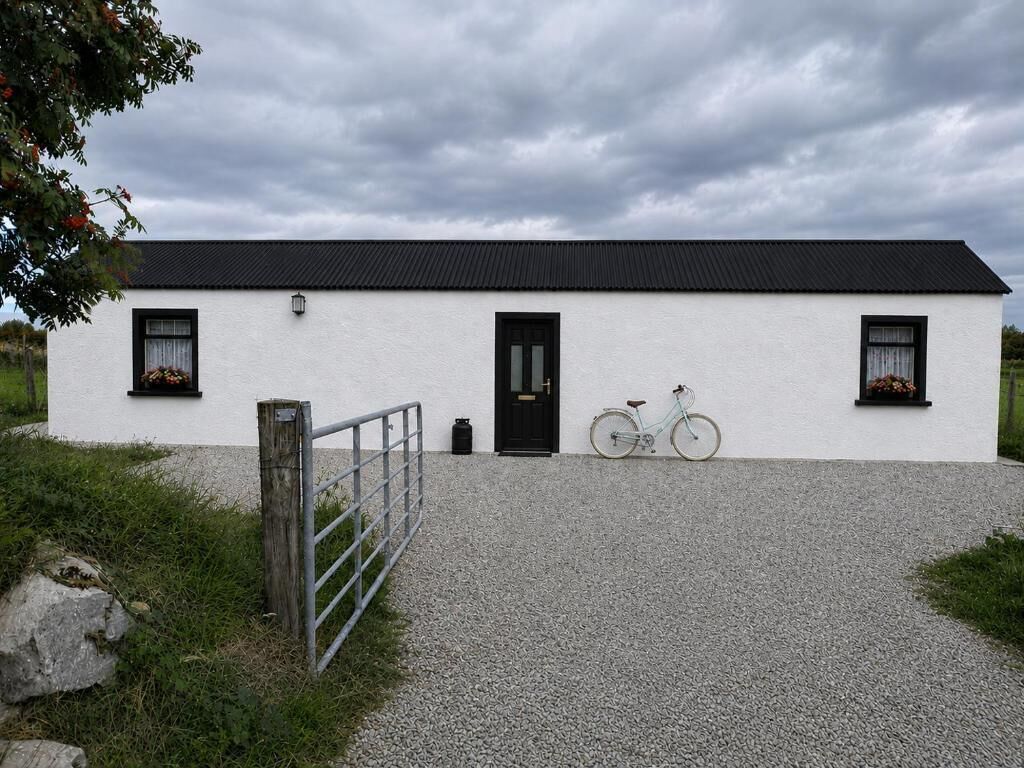 Un bâtiment blanc avec un toit noir, une allée en gravier et un vélo garé devant.