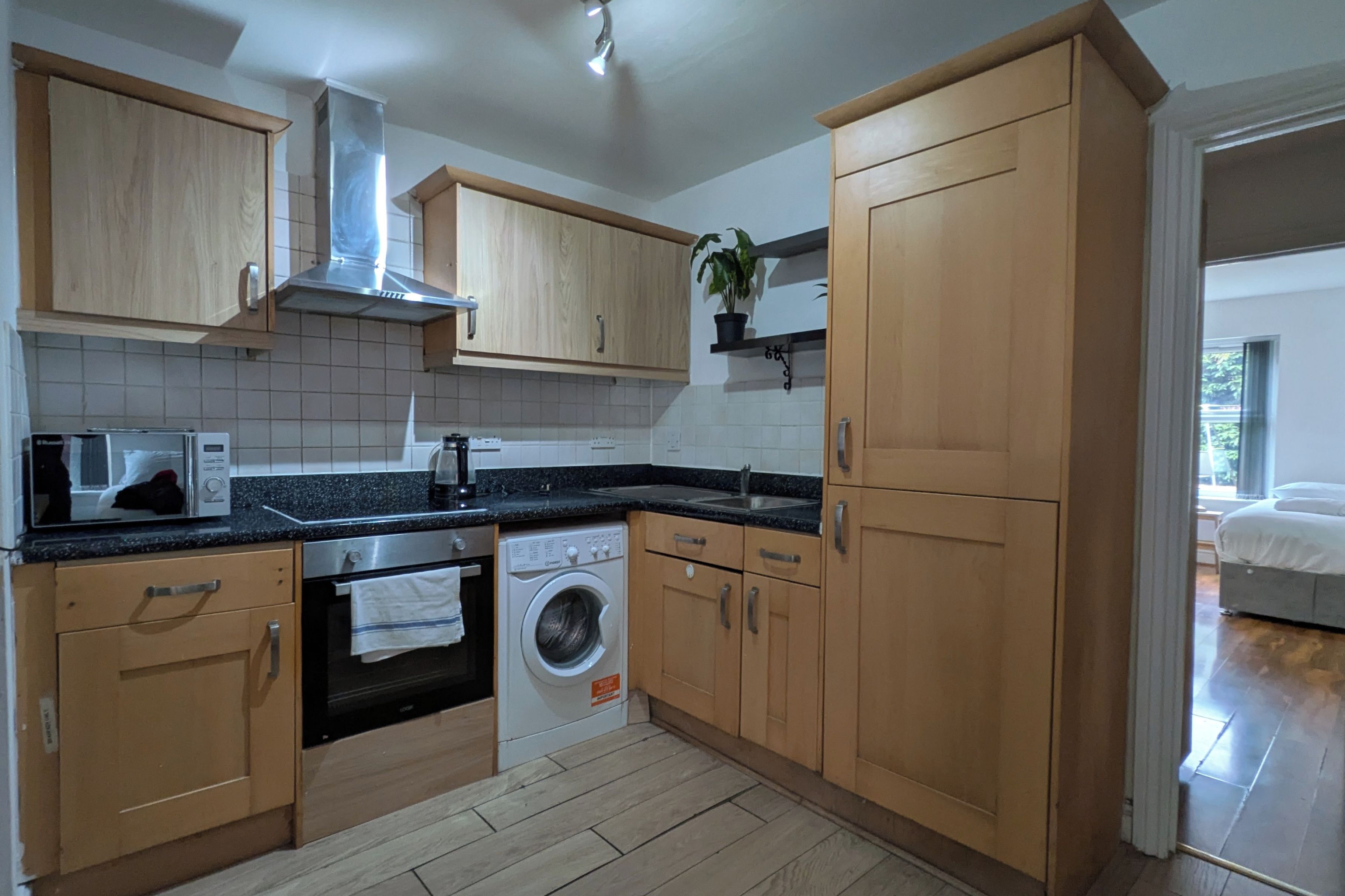 A modern kitchen with wooden cabinets, a built-in oven, a washing machine, and a microwave.