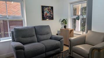 Un salon avec un canapé gris, un fauteuil beige, un tableau accroché au mur et une plante en pot.