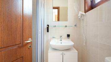 Un baño con puerta de madera, cabina de ducha con mampara de cristal, lavabo blanco con espejo y un inodoro.