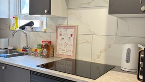 Een keuken met een marmeren achterwand, een kunstwerk met koffie als thema, een waterkoker en diverse keukenspullen.