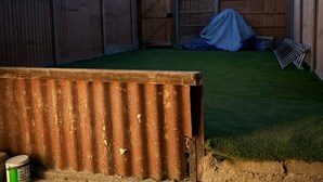 Een omheinde achtertuin met kunstgras, een overdekt terras en een metalen constructie.