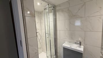 Une salle de bain moderne avec une douche à parois de verre, un lavabo blanc doté d’un robinet chromé et des murs à motifs de marbre.