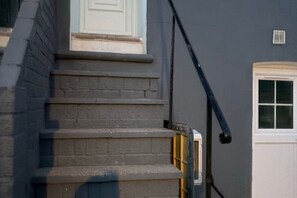 Eine Reihe von Betonstufen führen zu einer weißen Tür, an der Wand verläuft ein schwarzes Kabel.