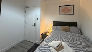 Een slaapkamer met een bed, nachtkastje, lamp en een deur.