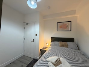 Ein Schlafzimmer mit einem Bett, einem Nachttisch, einer Lampe und einer Tür.
