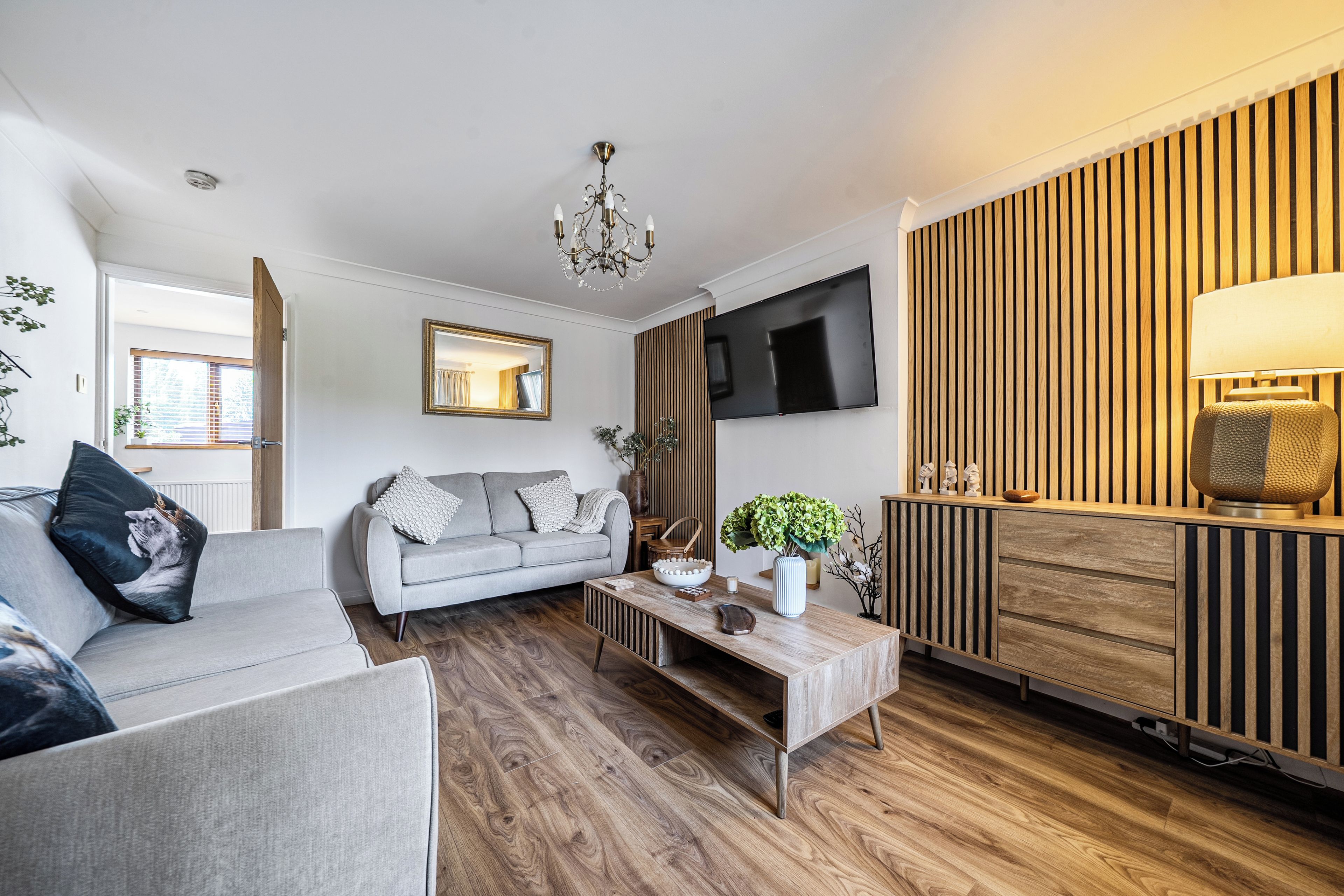 Ein modernes Wohnzimmer mit einem grauen Sofa, einem Holztisch und einem an der Wand montierten Fernseher.