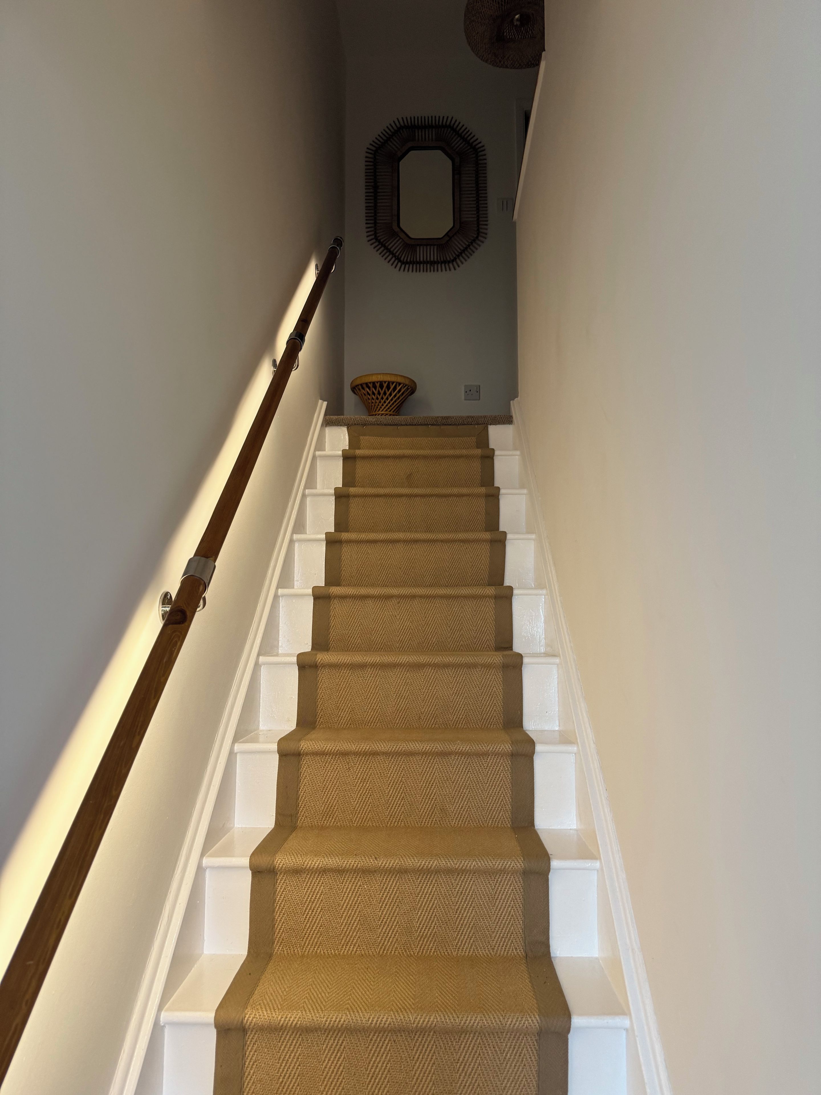 Una escalera con un estampado de espiga en la alfombra, peldaños blancos y barandilla de madera.