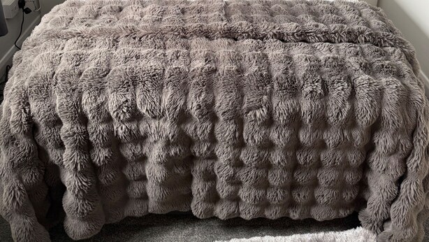 Una cama con edredón blanco y marrón con textura, dos lámparas de noche y un cabecero gris.