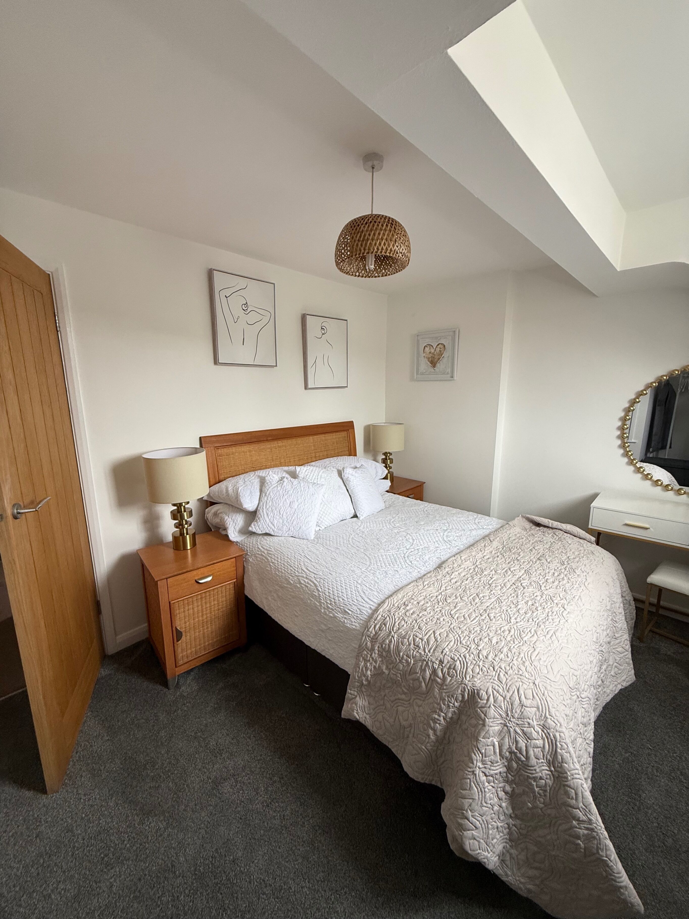 A bedroom with a bed, bedside tables, a desk, and a hanging light fixture.