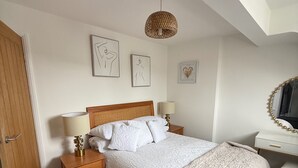 Un dormitorio con cama, mesitas de noche, un escritorio y una lámpara colgante.