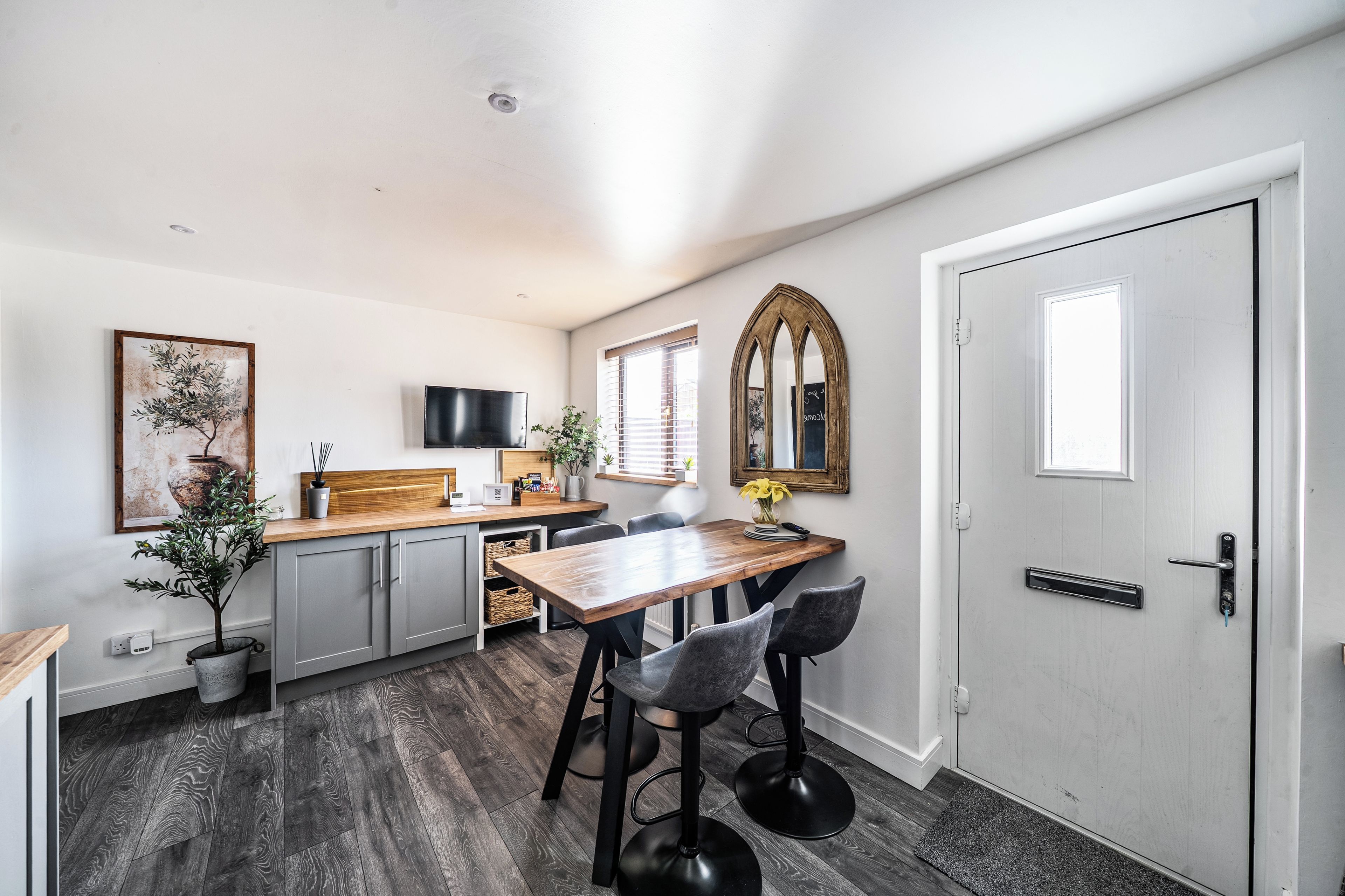 A modern kitchen with a wooden countertop, grey cabinets, and a dining area with a wooden table and bar stools.