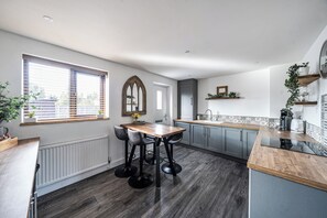 A modern kitchen with a dining area, featuring a wooden table, dark chairs, and a large window with blinds. - House Sleeps 4 with Parking and Garden (Scunthorpe)