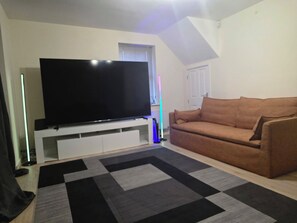A living room with a flat-screen TV on a stand, a brown sofa, and a patterned rug.