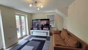Ein Wohnzimmer mit einem Flachbildfernseher, einem braunen Sofa, einem gemusterten Teppich und einem Deckenventilator.