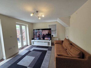 A living room with a flat-screen TV, a brown sofa, a patterned rug, and a ceiling fan. - Shirebrook 2-Bed Townhouse, with Free Parking, Ideal for Contractors and Families (Mansfield)