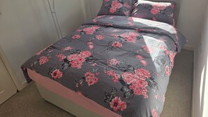 Ein Schlafzimmer mit einem Bett, floralem Bettzeug, einem roten Kleiderbügel und einem Fenster.