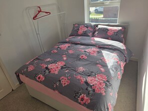 A bedroom with a bed, floral bedding, a red hanger, and a window. - Shirebrook 2-Bed Townhouse, with Free Parking, Ideal for Contractors and Families (Mansfield)