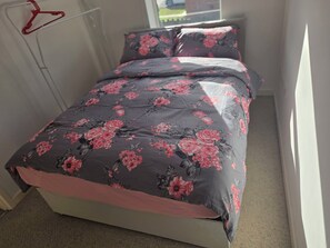 A bed with a floral bedspread and matching pillows in a room with a window. - Shirebrook 2-Bed Townhouse, with Free Parking, Ideal for Contractors and Families (Mansfield)