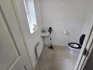 A small bathroom with a toilet, a sink, a window, and a radiator.