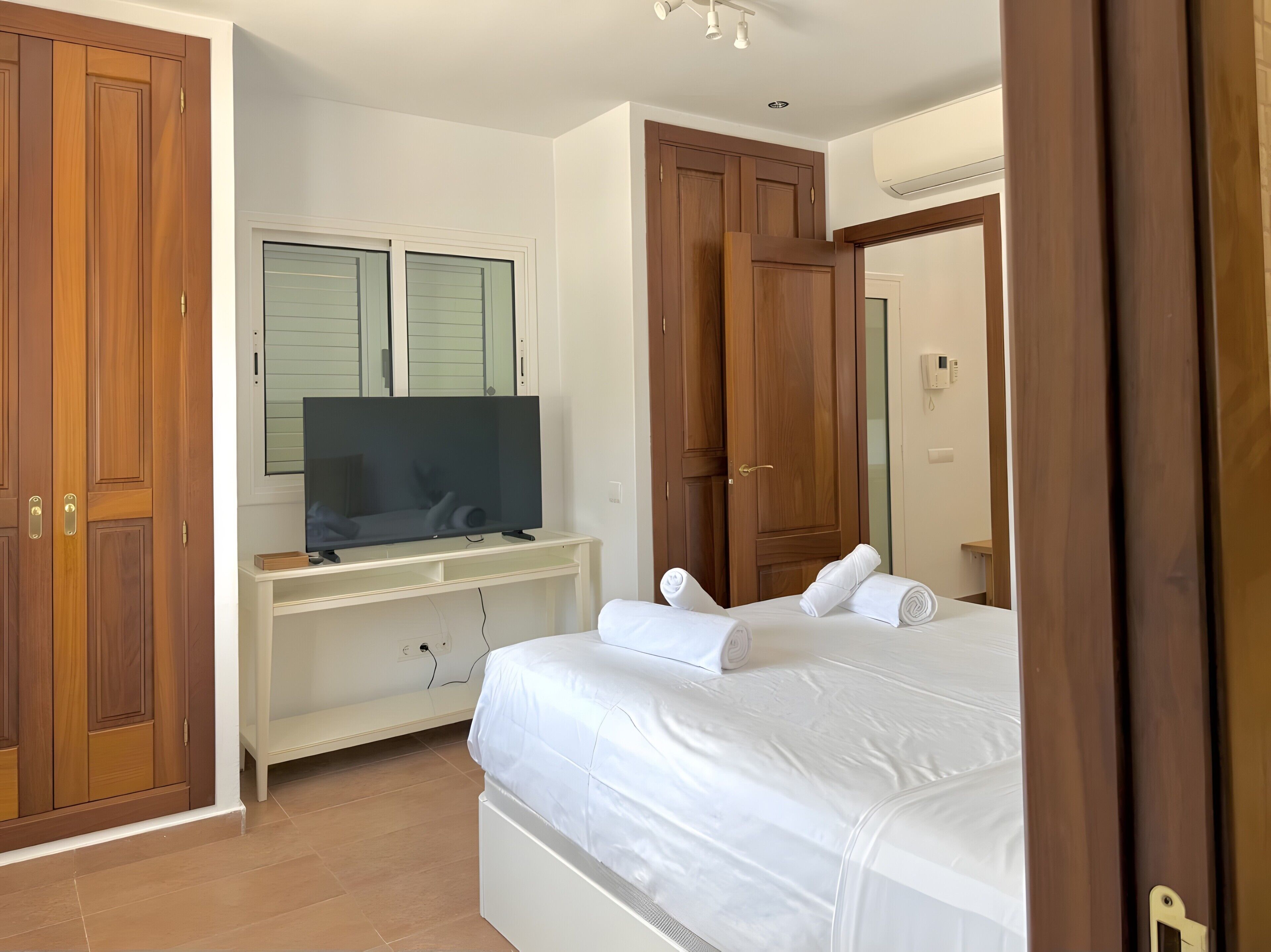 A bedroom with a bed, a television on a stand, wooden wardrobes, and a mirror.