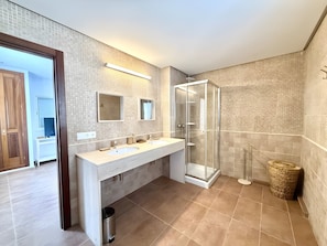 Een moderne badkamer met een douchecabine van glas, een wastafel met dubbele wastafel en een zichtbare prullenbak.