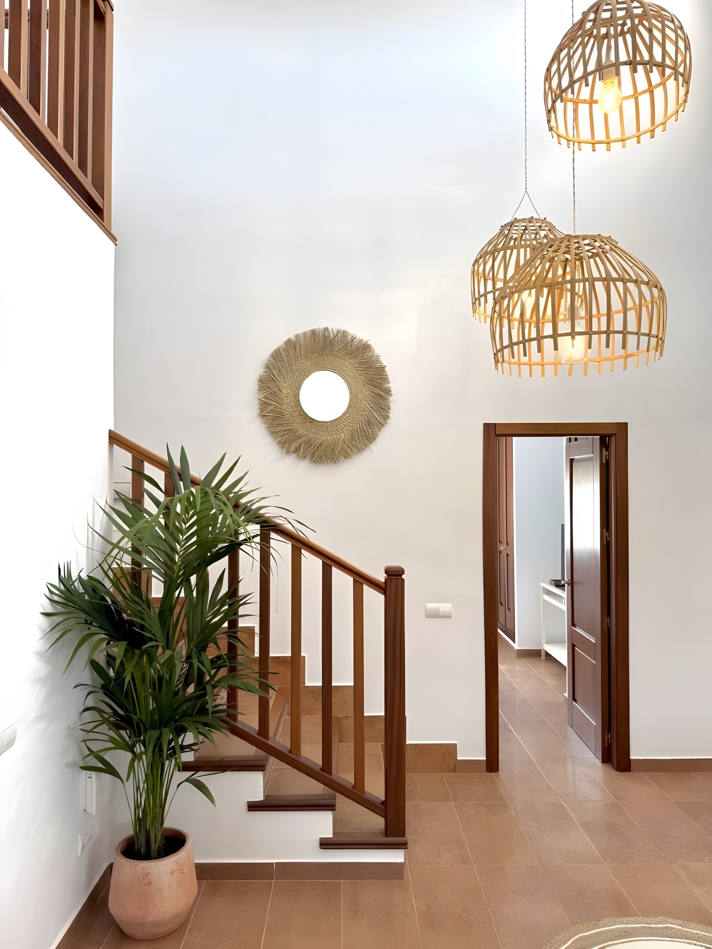 Een trap met houten leuningen, een bloempot, een ronde spiegel aan de muur en een hanglamp.