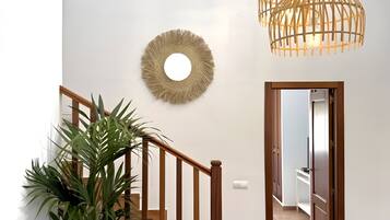 Een trap met houten leuningen, een bloempot, een ronde spiegel aan de muur en een hanglamp.