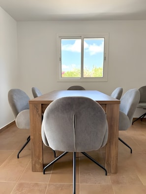 Een eetruimte met een houten tafel, grijs gestoffeerde stoelen en een raam met uitzicht op groen.