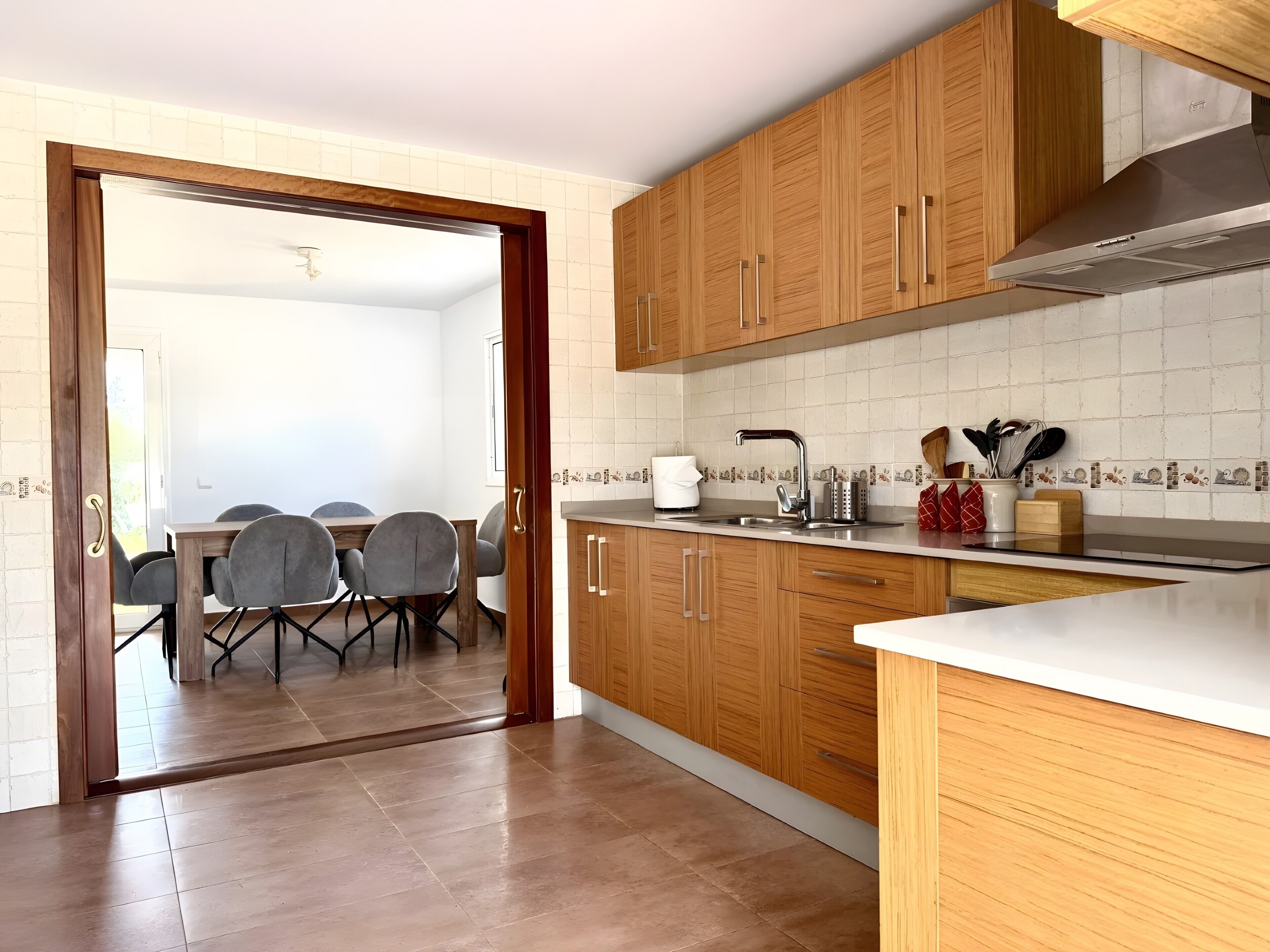 Een keuken met houten kastjes, een roestvrijstalen spoelbak en een eethoek met stoelen.