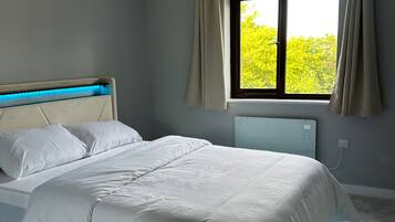A bedroom with a bed, a window with curtains, and a view of greenery outside.