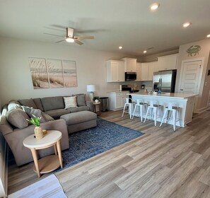 A modern kitchen with white cabinets, a stainless steel refrigerator, and a bar area with stools. - Gulf Views + Golf Cart & Pools! (Port St. Joe)