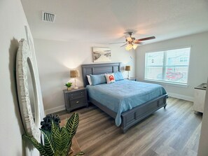 A bedroom with a bed, nightstands, a ceiling fan, a window with blinds, and a potted plant. - Gulf Views + Golf Cart & Pools! (Port St. Joe)