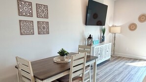 Een eetgedeelte met een houten tafel en stoelen, een geweven vloerkleed en een flatscreen aan de muur.