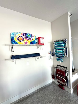 A room with a wall-mounted shelf holding a colorful tie-dye pillow, a blue blanket, and a box of ULINE wipes. - Gulf Views + Golf Cart & Pools! (Port St. Joe)