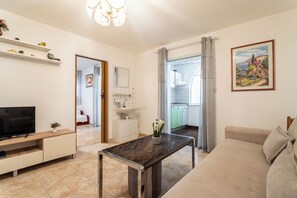 Ein modernes Wohnzimmer mit Flachbildfernseher, Esstisch, Sofa und einer durchgehenden Tür erkennbaren Küche.