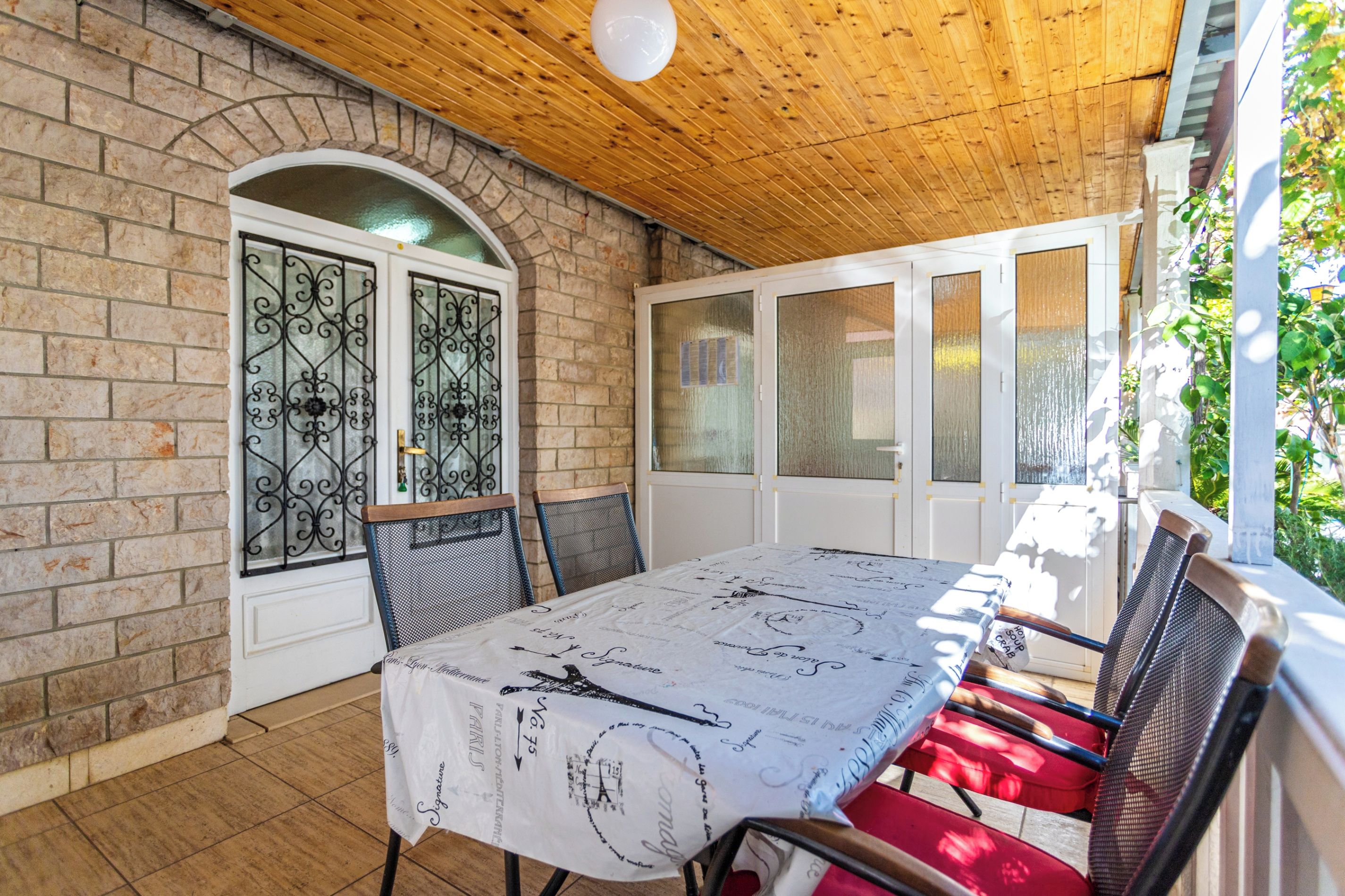 Een overdekt terras met een eettafel, een bakstenen muur en een houten plafond.